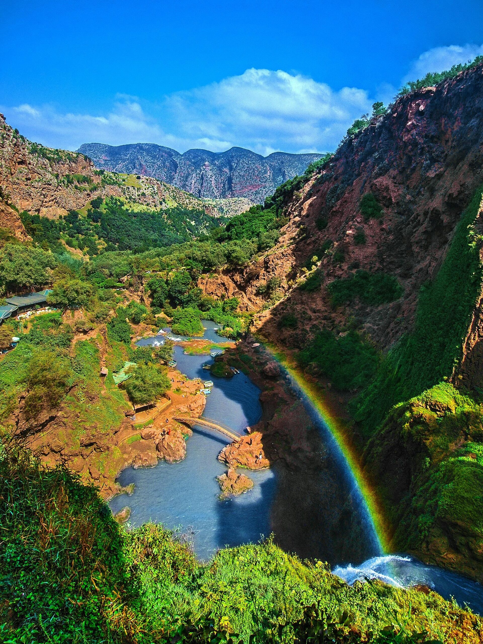 Ouzoud Waterfalls: Aerial view of a lush valley, with a rainbow arching over the flowing river and rocky cliffs.