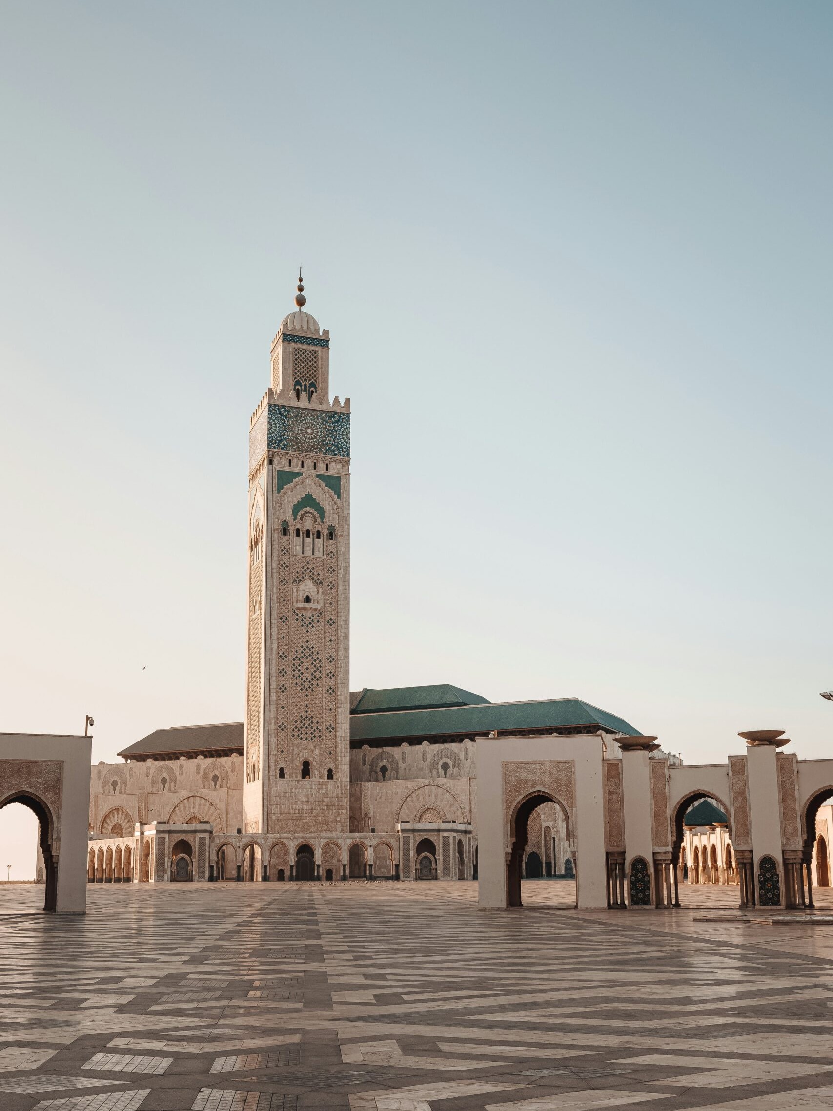 The majestic Hassan II Mosque in Casablanca, Morocco, with a towering minaret and intricate details, bathed in warm sunlight.